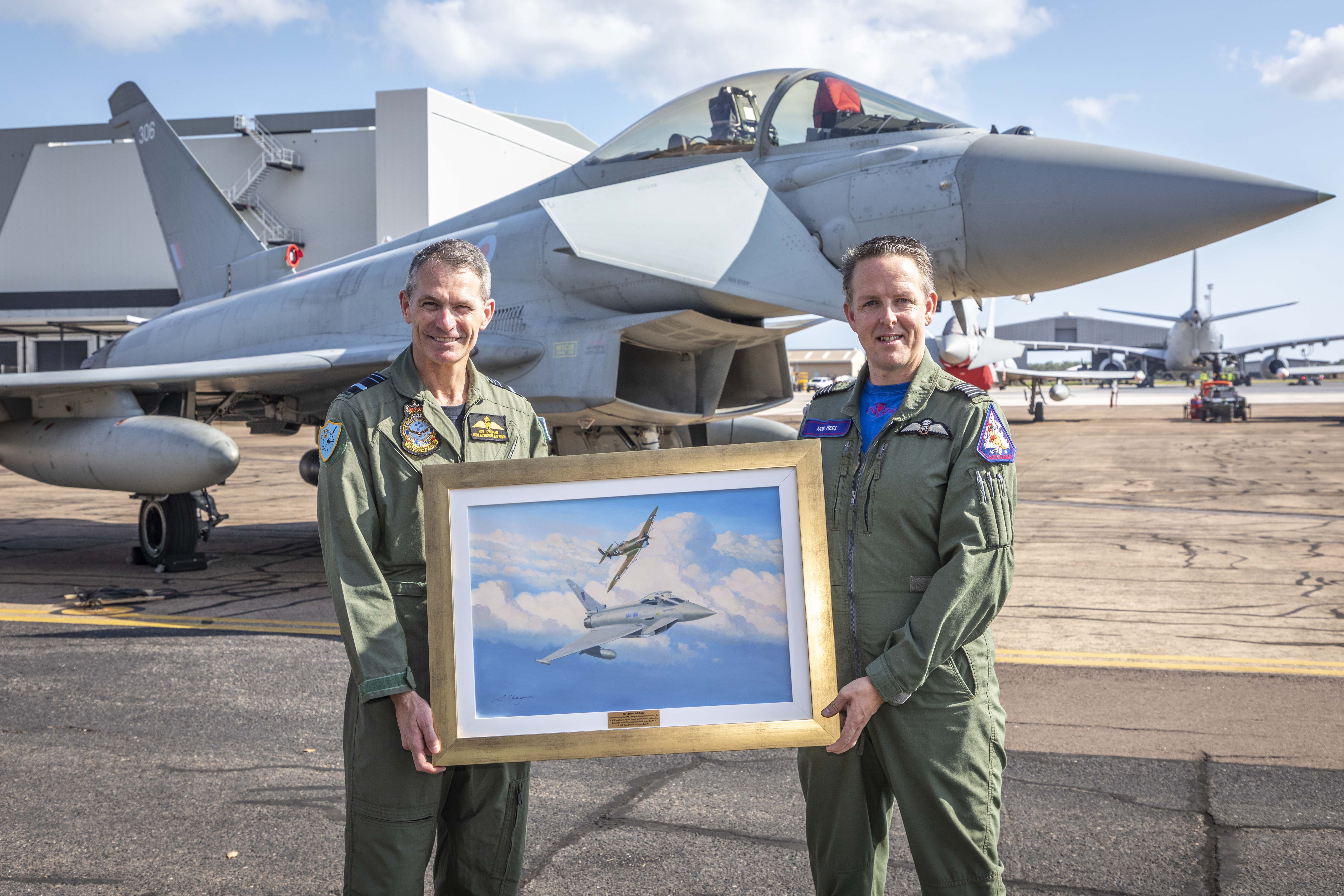 Image shows RAF Personnel with Typhoon on the airfield. They hold a painting of two flying Typhoons.